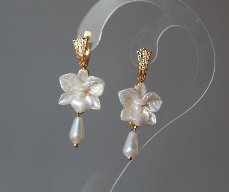 May include: A pair of gold earrings with white flower charms and pearl drops.