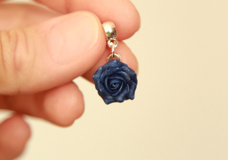 May include: A dark blue rose charm with a silver bail. The rose is made of polymer clay and has a shiny finish.