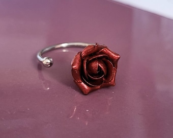 May include: A silver ring with a red rose-shaped design. The rose is made of metal and has a textured surface.