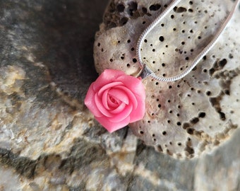 May include: A delicate silver chain necklace with a pink polymer clay rose pendant. The rose is detailed with a layered design and a realistic appearance.