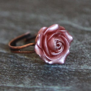 May include: A rose-colored ring with a delicate rose design. The ring is made of copper and has a simple band.