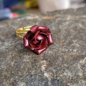 May include: A gold adjustable ring with a burgundy rose flower design.