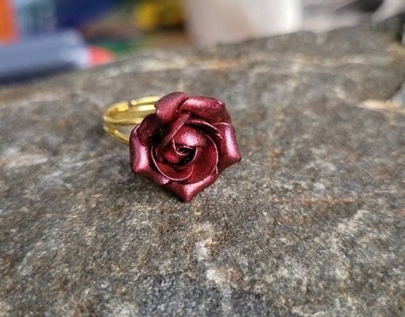 May include: A gold adjustable ring with a burgundy rose flower design.