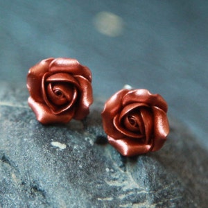 Può includere: Un paio di orecchini a bottone a forma di rosa color rame. Gli orecchini sono realizzati in pasta polimerica e hanno un design di rosa realistico.