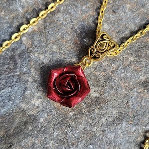 May include: A gold chain necklace with a red rose pendant. The rose is detailed and has a metallic finish.