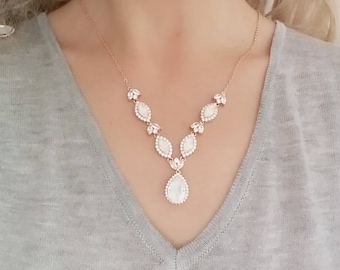 Puede incluir: Un collar de oro rosa con un colgante en forma de lágrima y una cadena delicada. El colgante está adornado con piedras de circonita cúbica transparentes, creando un efecto brillante. El collar es perfecto para una boda u otra ocasión especial.