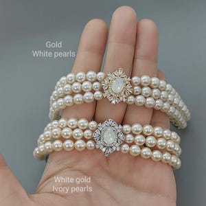 May include: Two pearl necklaces with a decorative clasp. The top necklace has gold colored clasps and white pearls. The bottom necklace has silver colored clasps and ivory pearls.  The text "Gold White pearls" is above the top necklace and the text "White gold Ivory pearls" is below the bottom necklace.