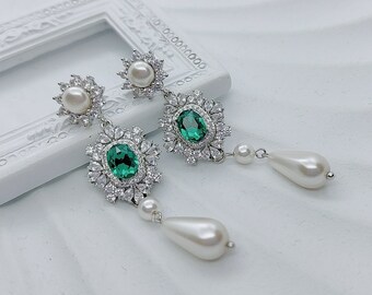 May include: A pair of silver earrings with green oval gemstones surrounded by clear rhinestones. Each earring has a pearl drop and a smaller pearl at the top.