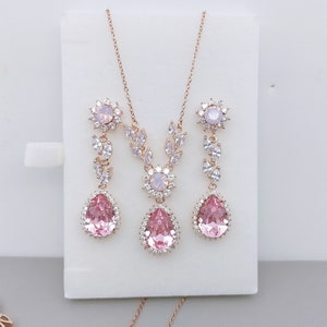 Puede incluir: Un collar y pendientes de oro rosa con detalles de cristal rosa y blanco. El collar presenta un delicado dise&ntilde;o floral con un colgante en forma de l&aacute;grima. Los pendientes tienen un dise&ntilde;o similar con un colgante en forma de l&aacute;grima m&aacute;s peque&ntilde;o.