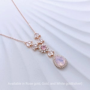 Könnte beinhalten: Halskette aus Roségold mit einem tropfenförmigen, hellrosa Anhänger. Der Anhänger ist von einem Kranz aus kleinen, klaren Kristallen umgeben. Die Halskette hat ein Blumendesign mit klaren Kristallen und einem kleinen rosa Mittelstein. Der Text unten lautet "Available in Rose gold, Gold, and White gold(silver)".