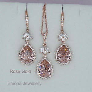 May include: Rose gold bridal jewelry set with teardrop shaped blush pink crystals and clear rhinestones. The set includes a necklace and earrings.
