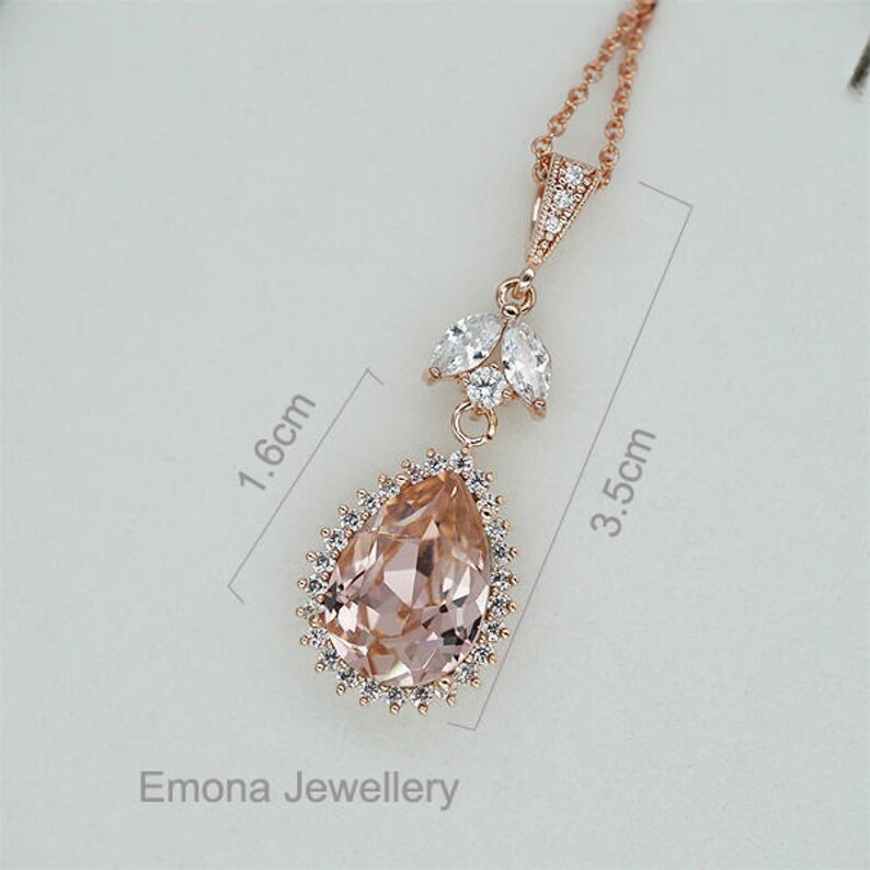 May include: A rose gold pendant necklace with a large pear-shaped pink crystal surrounded by smaller clear crystals. The pendant measures 3.5 inches in length and 1.6 inches in width.  Emona Jewellery.