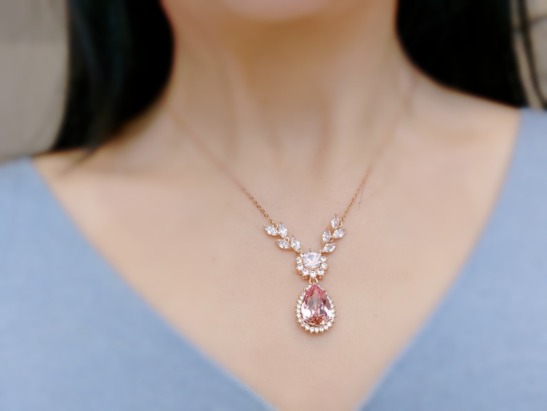 Puede incluir: Un delicado collar de oro con un colgante de piedra preciosa rosa en forma de pera rodeado de peque&ntilde;as piedras preciosas transparentes. El collar presenta un dise&ntilde;o en forma de hoja con piedras preciosas transparentes.
