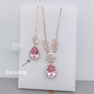 Puede incluir: Un conjunto de collar y pendientes de oro rosa con un colgante de cristal rosa en forma de l&aacute;grima y un dise&ntilde;o floral. El collar tiene una cadena delicada y los pendientes son de estilo gota.