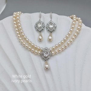 May include: A two-strand pearl choker necklace with a teardrop pendant and matching earrings. The pendant and earrings feature a white gold setting with clear rhinestones. The text "White gold ivory pearls" is visible below the necklace.