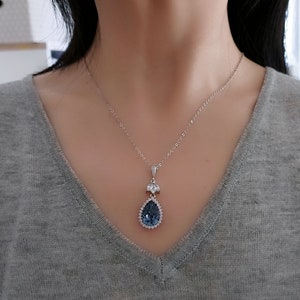 Op de afbeelding: Een zilveren ketting met een traanvormige hanger met een grote blauwe kristal omringd door kleinere heldere kristallen.