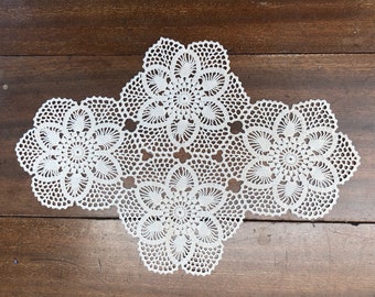 May include: White crocheted doily with a floral design. The doily is made of delicate lace and has a scalloped edge.