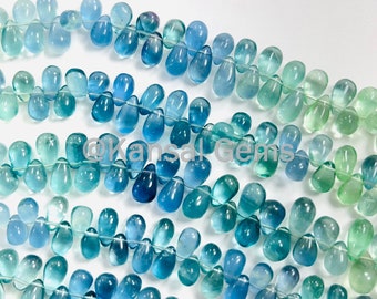 May include: A strand of blue and green gemstone beads in a teardrop shape. The beads are strung on a clear thread and are arranged in a graduated pattern, with the darkest blue beads at the top and the lightest green beads at the bottom.
