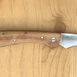 Op de afbeelding: Een mes met een houten handvat, een gebogen lemmet en een draadborstel bevestigd aan het handvat.