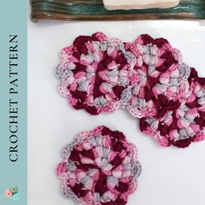 May include: Four crocheted coasters in shades of pink, burgundy, and grey. The coasters are circular and have a flower-like design.
