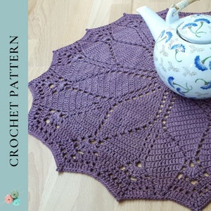 May include: A purple crochet doily with a delicate lace pattern. The doily is round and has a scalloped edge. It is sitting on a wooden surface.
