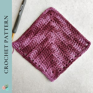 May include: A square, crocheted item in shades of purple and burgundy, with a textured stitch pattern. A crochet hook is visible, along with the text "CROCHET PATTERN". The item appears to be a washcloth or small blanket.