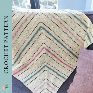 May include: A crocheted blanket with a diagonal pattern in white, pink, and teal. The blanket is made with a textured stitch and has a fringe border.