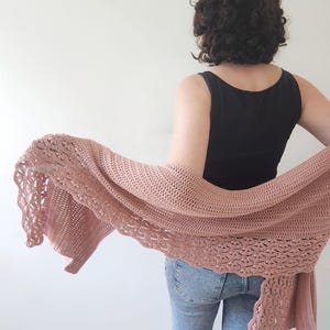 K&ouml;nnte beinhalten: Ein altrosa geh&auml;kelter Schal mit einem gewellten Rand. Der Schal besteht aus einem weichen, offen gewebten Material. Die Person im Bild tr&auml;gt ein schwarzes Tanktop und blaue Jeans.