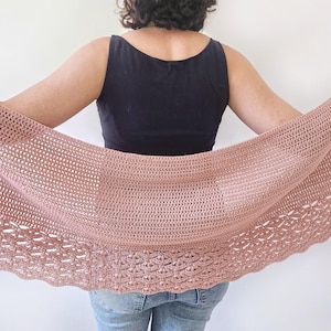 K&ouml;nnte beinhalten: Ein altrosa geh&auml;kelter Schal mit gewelltem Rand wird gezeigt. Der Schal wird offen gehalten und zeigt ein schwarzes Tanktop und blaue Jeans. Das H&auml;kelmuster ist sichtbar und zeigt die Textur und das Design des handgefertigten Accessoires.