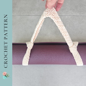 Puede incluir: Un tapete de yoga morado con una correa de crochet blanca unida a los extremos. La correa está pasada por el tapete y sostenida por una mano.