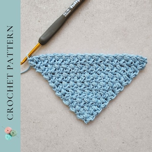 May include: A blue crocheted triangle with a crochet hook on a gray surface.