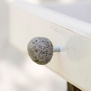 Könnte beinhalten: Nahaufnahme einer grauen Steingriff, die an einer weiß lackierten Schublade befestigt ist.