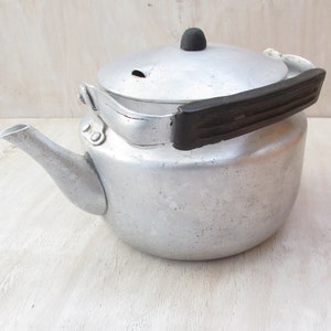 Könnte beinhalten: Eine silberne Aluminium-Teekanne mit schwarzem Griff und Deckel. Die Teekanne hat einen Ausguss und ein kleines Loch im Deckel.