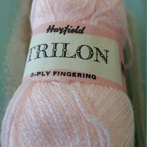 Könnte beinhalten: Eine rosa Garnrolle mit einem weißen Etikett, auf dem "Haryfield TRILON 3-PLY FINGERING" steht.