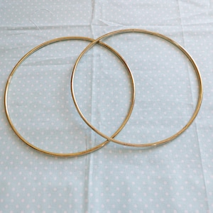 Può includere: Due cerchi metallici color oro, sovrapposti, sono esposti su un tessuto azzurro chiaro con un motivo a pois bianchi. I cerchi sono circolari e sembrano essere fatti di metallo sottile.