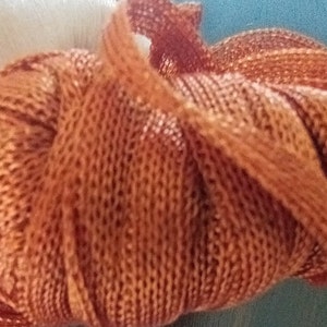 May include: A close-up of a ball of rust-coloured yarn. The yarn is made of a soft, textured material and has a slightly fuzzy appearance.