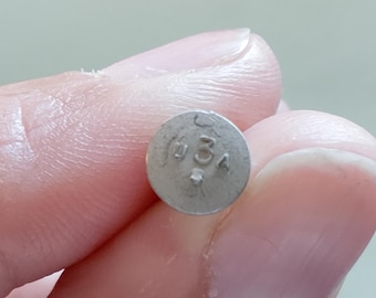 May include: A small, round, silver-colored tablet with the imprinted text "USA 3A". The tablet is held between two fingers, with a blurred background.
