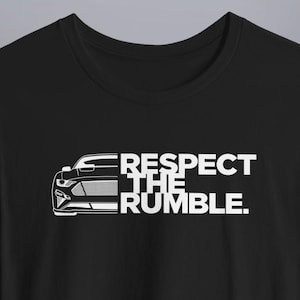 May include: Black t-shirt with a white graphic of a car's front end and the text "RESPECT THE RUMBLE." The design features a detailed illustration of the car's headlights, grille, and bumper.