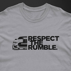 May include: A light gray t-shirt featuring a black graphic of a car and the text "RESPECT THE RUMBLE." The car graphic is a stylized front view of a sports car.