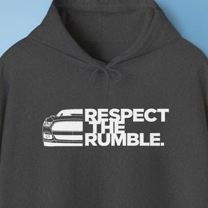 May include: A dark charcoal gray hooded sweatshirt featuring a white graphic print on the chest. The design includes a partial front view of a car and the text "RESPECT THE RUMBLE." The hoodie has a drawstring hood and long sleeves.