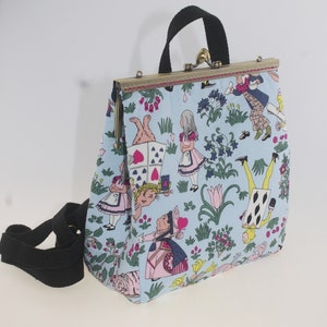 May include: A light blue canvas purse with a clasp closure and a long adjustable strap. The purse features a whimsical print of Alice in Wonderland characters and playing cards.