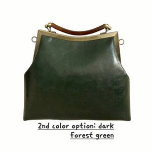 May include: Dark forest green handbag with a curved wooden handle and brass-colored metal frame. The bag has a structured shape and a clasp closure. The text at the bottom reads "2nd color option: dark forest green."