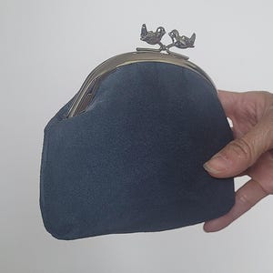 May include: A dark blue suede coin purse featuring a metallic kiss-lock closure. The clasp is designed with two small, detailed silver-toned birds perched on a branch, serving as the opening mechanism for the soft, textured fabric pouch.