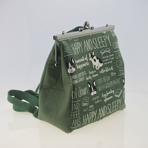 May include: A green fabric coin purse with a silver clasp. The purse has a white print of a dog, coffee cups, and text that says "ANS HAPPY AND SLEEPY" and "ol down".