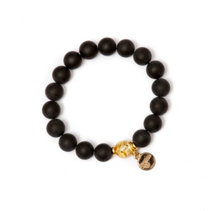 May include: A black beaded bracelet with a gold charm. The beads are matte and the charm has a textured design.