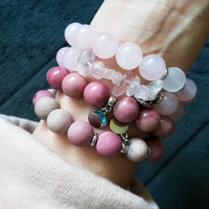 Pode incluir: Quatro pulseiras empilhadas feitas de pedras de quartzo rosa e rosa. A pulseira superior é feita de pedras grandes, lisas e redondas. A segunda pulseira é feita de pedras menores de forma irregular. As duas pulseiras inferiores são feitas de pedras lisas e redondas.