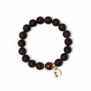 Könnte beinhalten: Schwarzes Perlenarmband mit einem braunen Tigerauge-Perle und einem silbernen Anhänger. Der Anhänger trägt die Gravur "Zen".