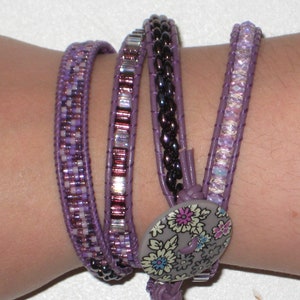 May include: A multi-strand bracelet with purple, white, and silver beads. The bracelet has a floral button closure.