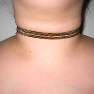 May include: A brown choker necklace with a thin gold stripe.