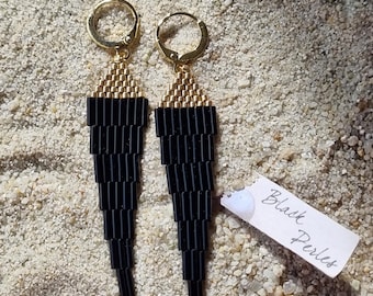May include: A pair of black beaded earrings with gold-colored hoops and accents. The earrings are long and tapered, with a geometric design. The text "Black Perles" is on a small tag.